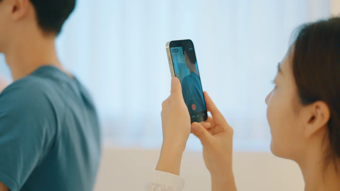 커튼 창가에 선 회원의 뒤쪽 옆모습을 휴대폰으로 찍는 강사